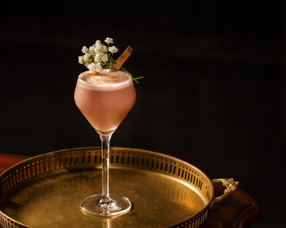 Image of the Pink Squirrel cocktail at Roosevelt Room sitting on a golden tray with a dark background.
