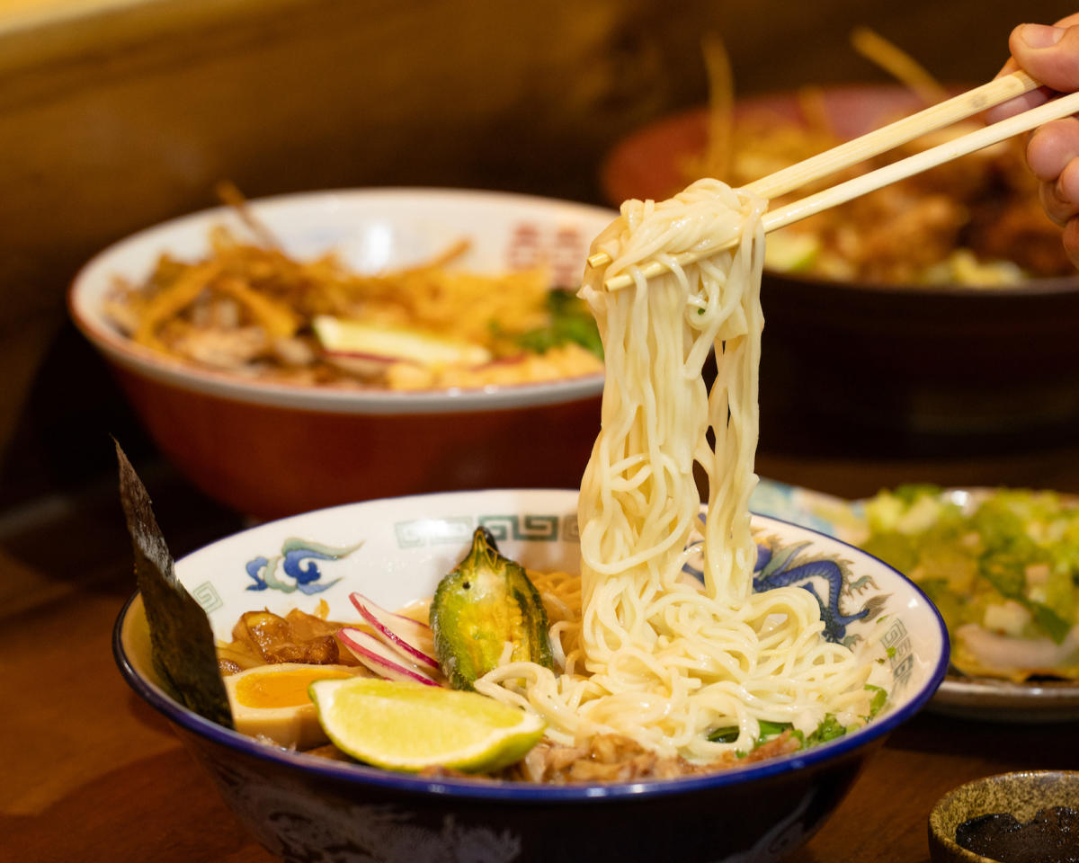 Image of a bowl of ramen with someone holding a bunch of noodles with chopsticks above the bowl.