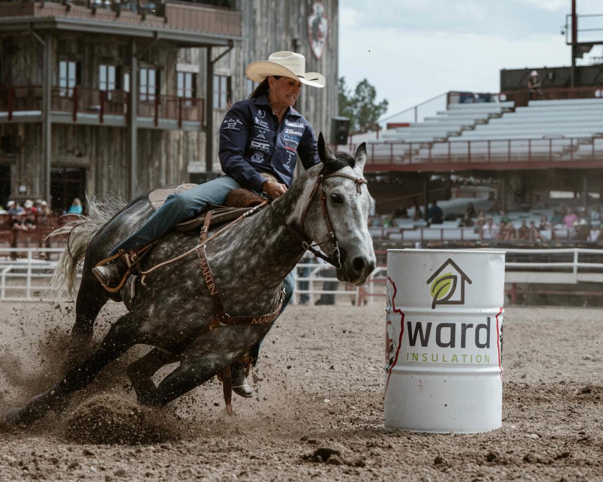 A rodeo cowgirl rounds a barrel on a horse during a fast-paced barrel race.