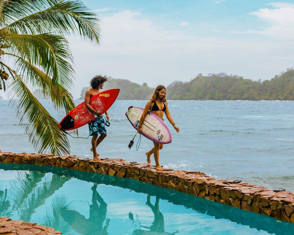 Couple walking near a pool with surfboards, Isla Grande beach can be seen in the background