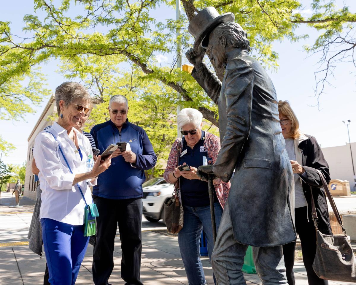 A group of four older adults gather around a Presidential-statue. They are participating in the audio tour.