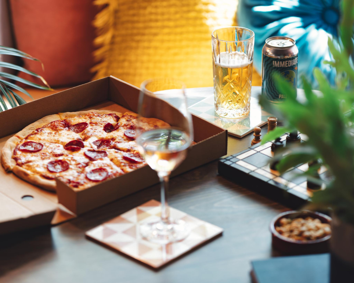 Pepperoni pizza in open cardboard box next two a glass of wine and can of beer