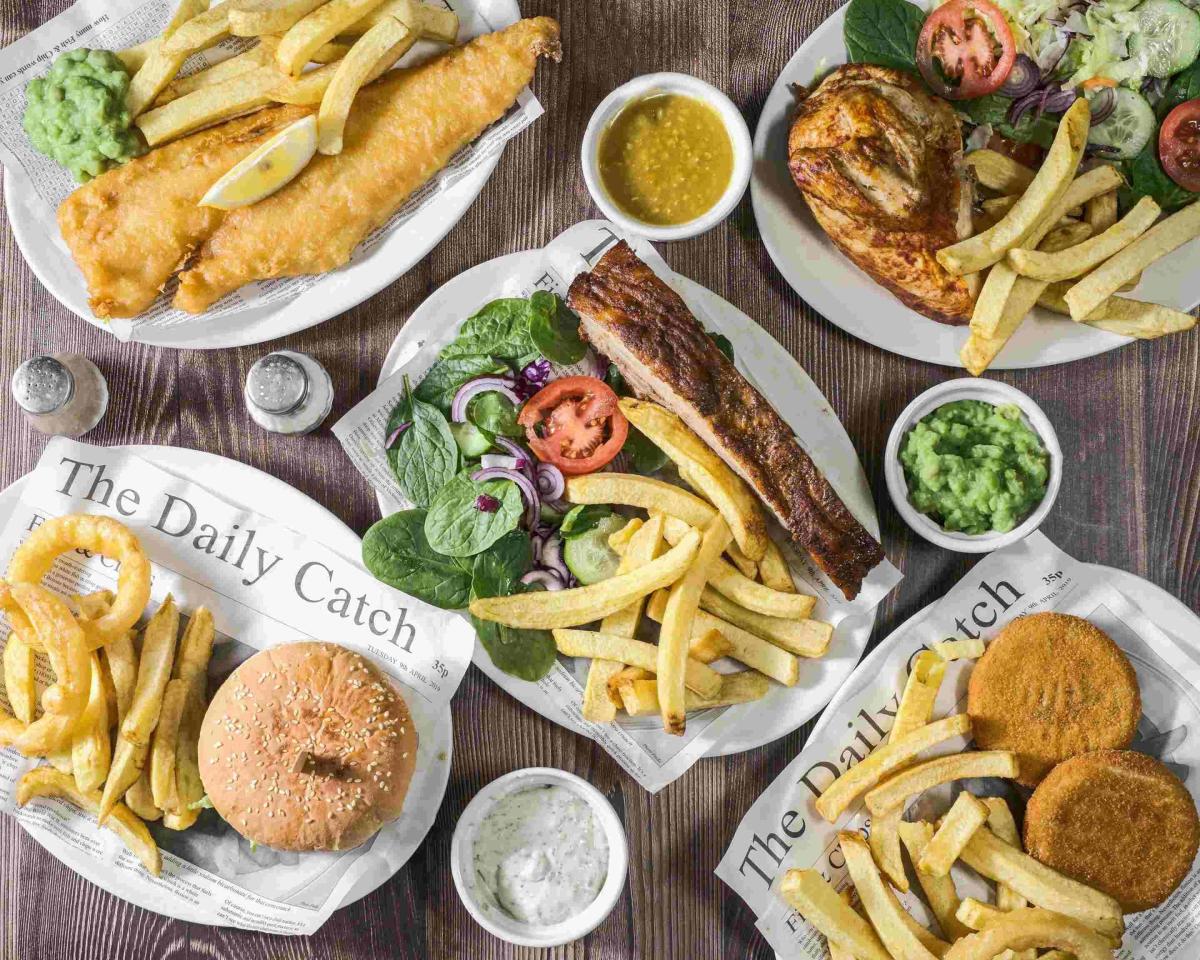 The Fish Station dishes on white plates including ribs, chips and salad, burger, fish cakes, chicken breast and battered fish