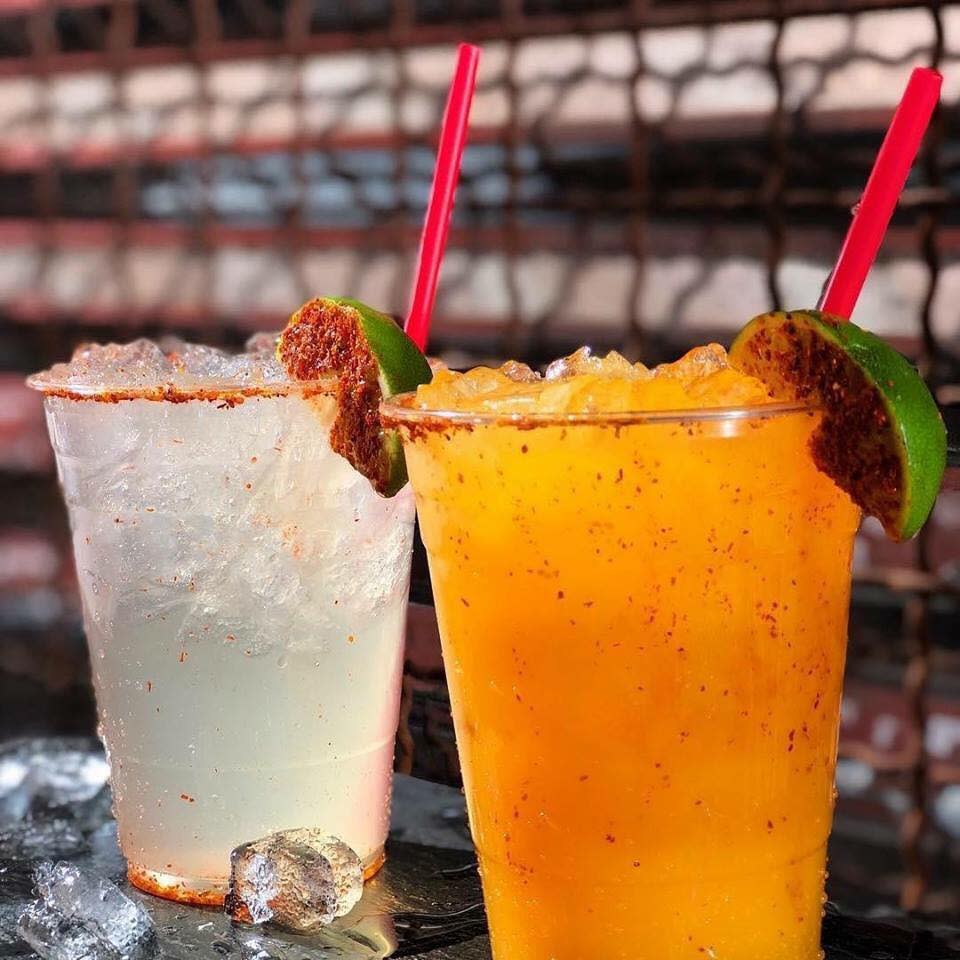 Two cocktails on a bar close up. One is a yellowish white, the other is orange.