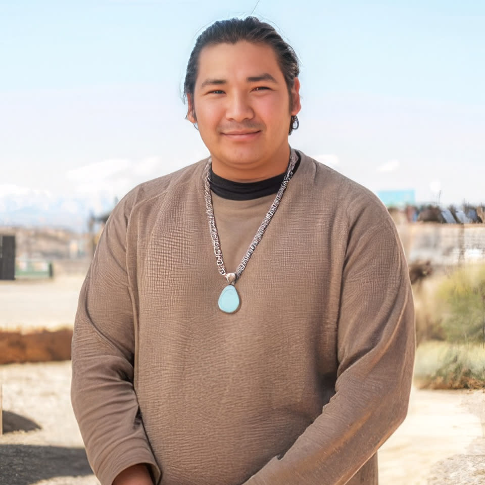 Person standing outdoors wearing a pendant necklace.
