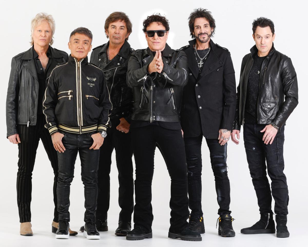 Members of the band Journey pose for a photo wearing all black against a white backdrop.