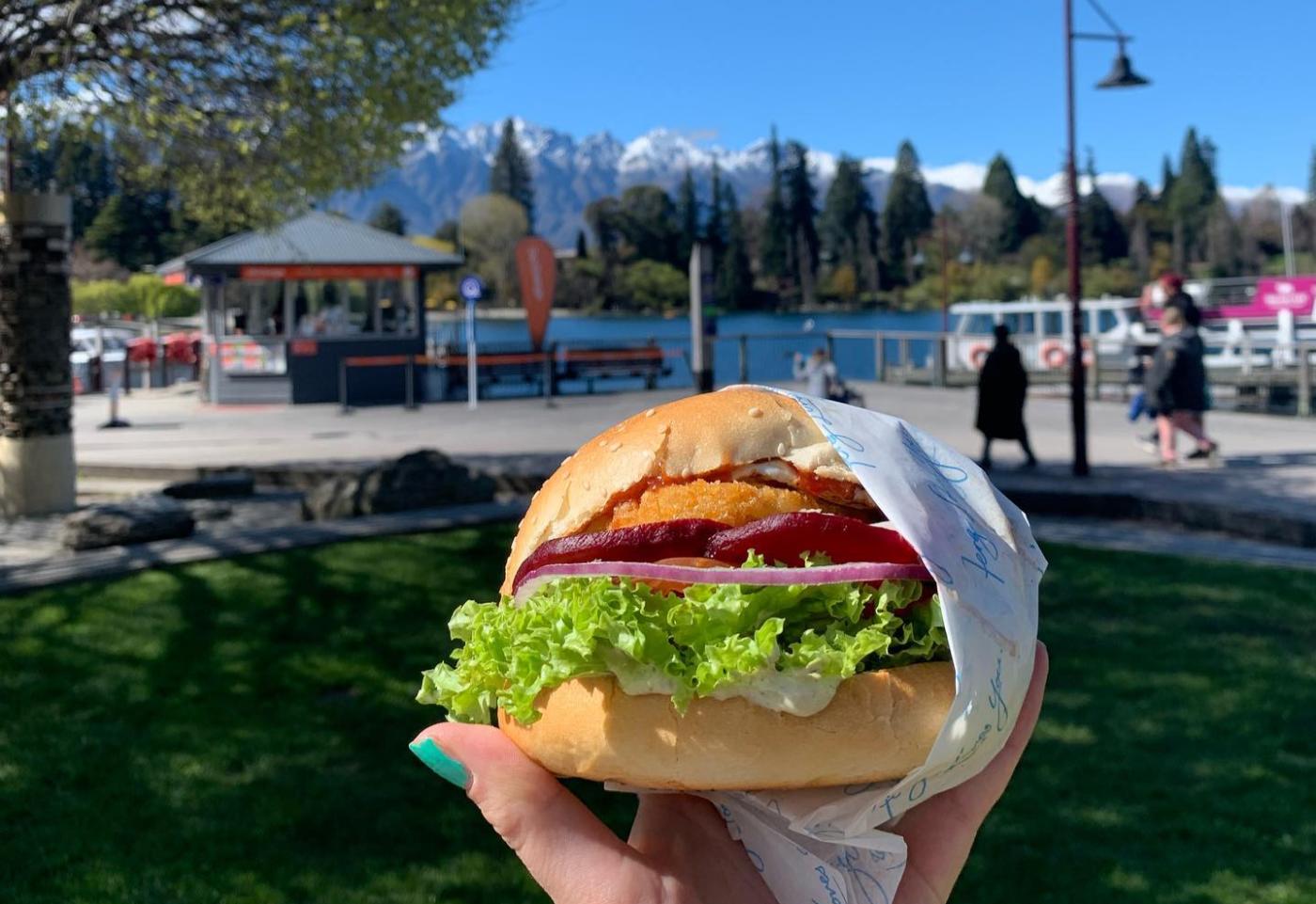 Holding a fergburger with view of the Remarkables mountains in the background