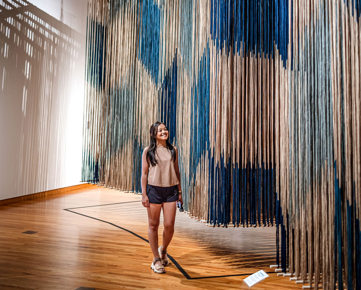 Woman walking in front of blue and white hanging tapestries at Fort Wayne Museum of Art