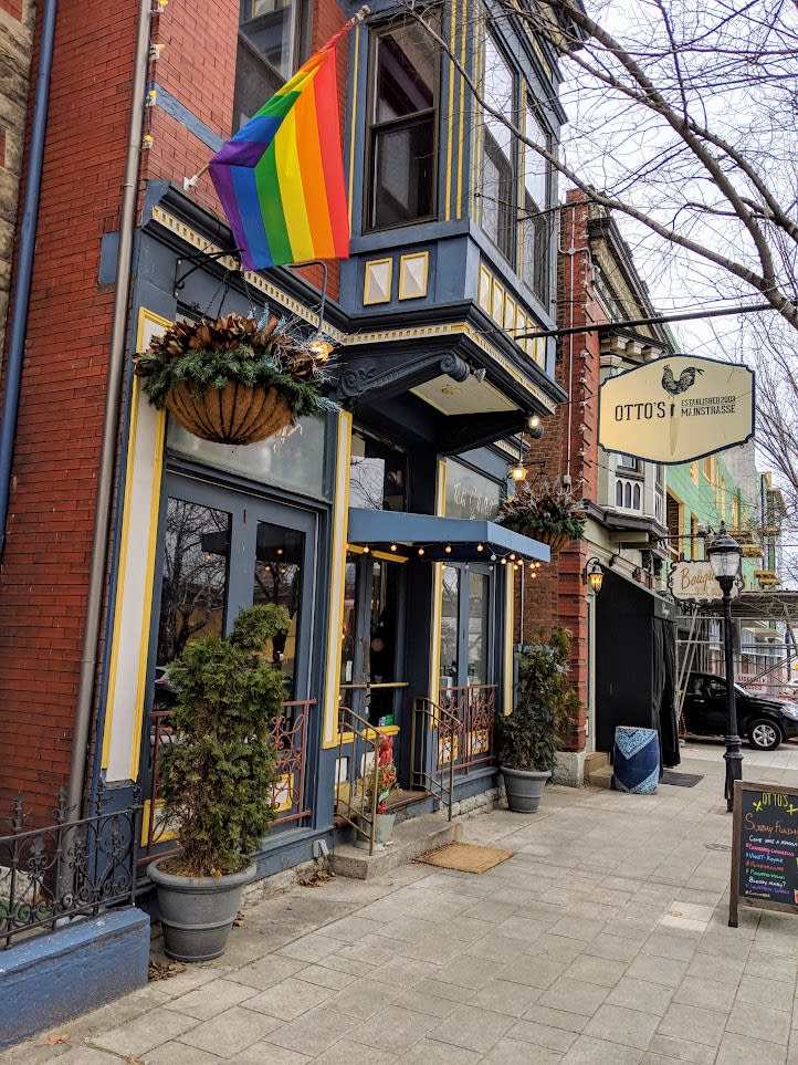 A Pride flag and flower baskets hanging in front of the brick building that houses Otto's restaurant in Covington, Ky.
