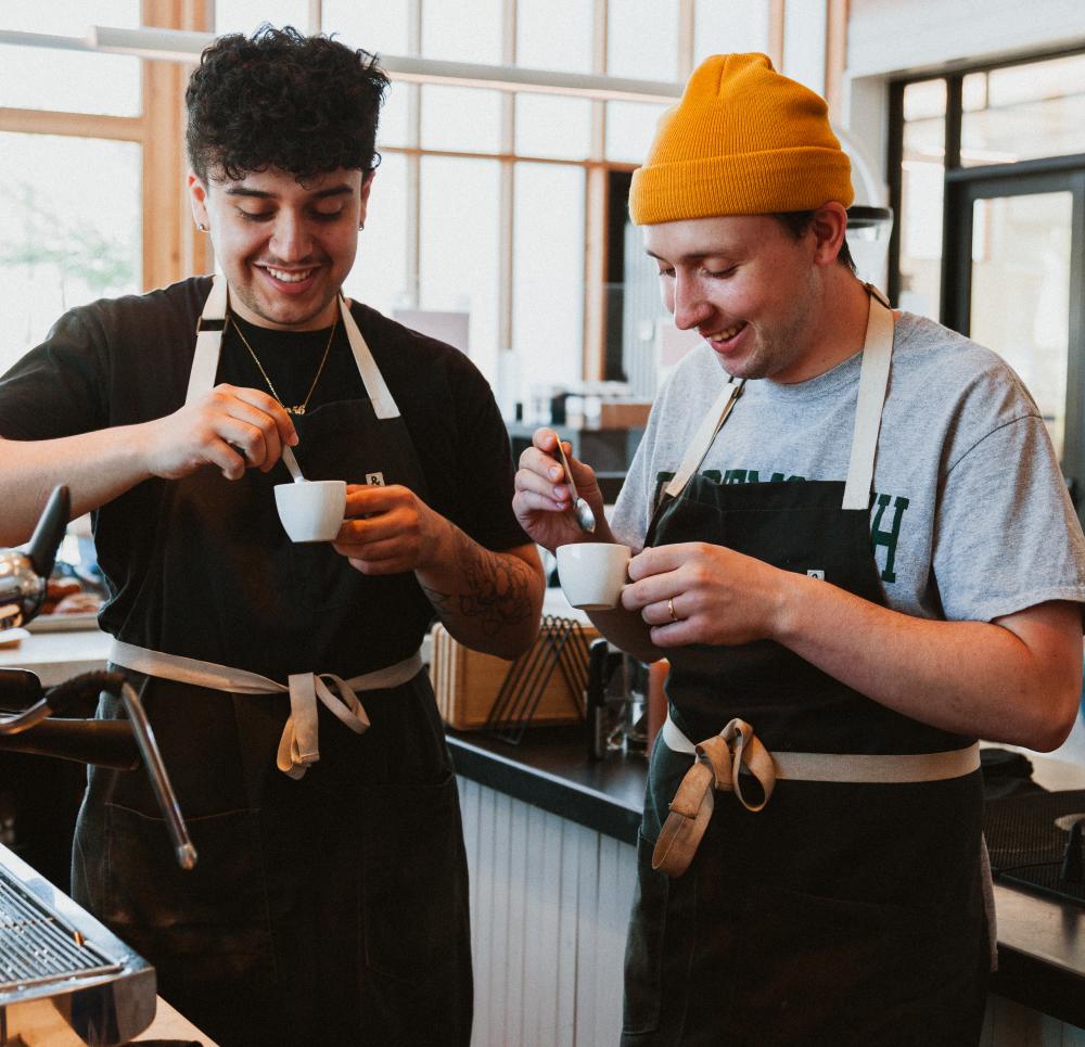 Two men standing behind coffee bar, admiring small cups of espresso.