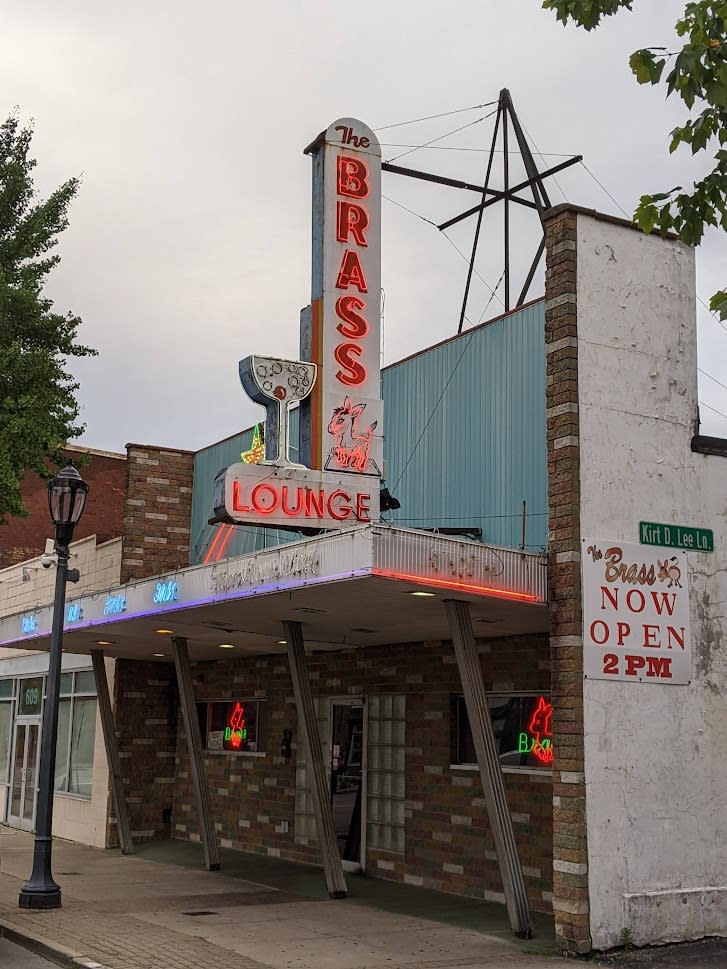 Image is of a side, front view of the Brass Ass building, including the neon sign above the canopy.