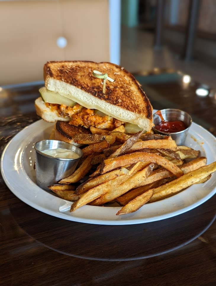 Image is of a crispy, buffalo chicken sandwich on sourdough toast with french fries on the side.