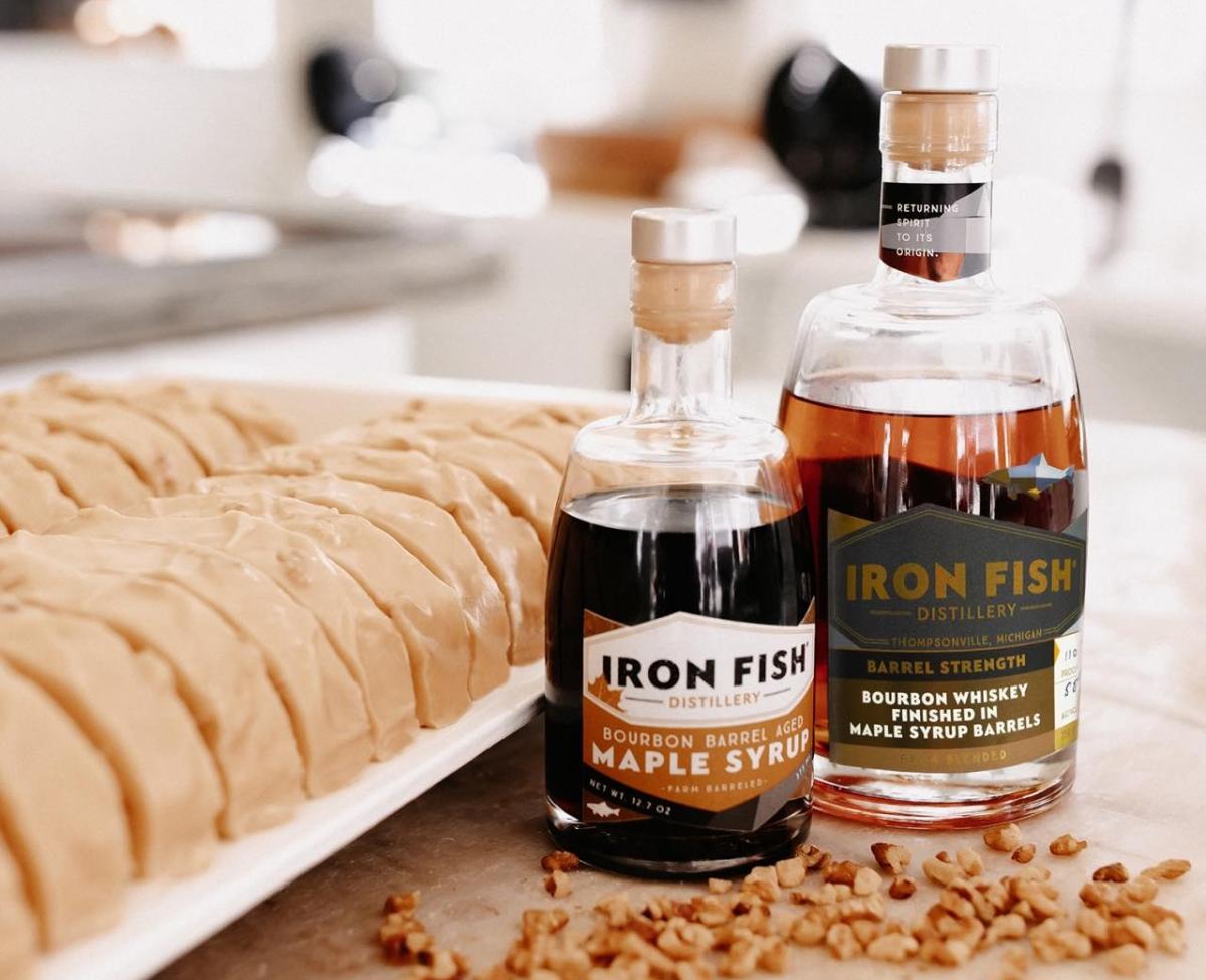 Bottles of Iron Fish Distillery bourbon barrel aged maple syrup and bourbon whiskey next to slices of Mackinac Island fudge