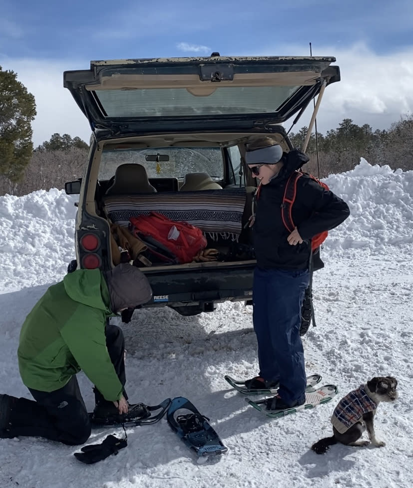 Two people behind a car putting snowshoes on
