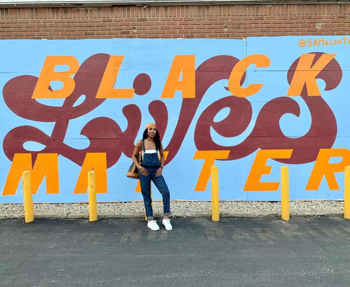 Girl poses in front of Black Lives Matter mural
