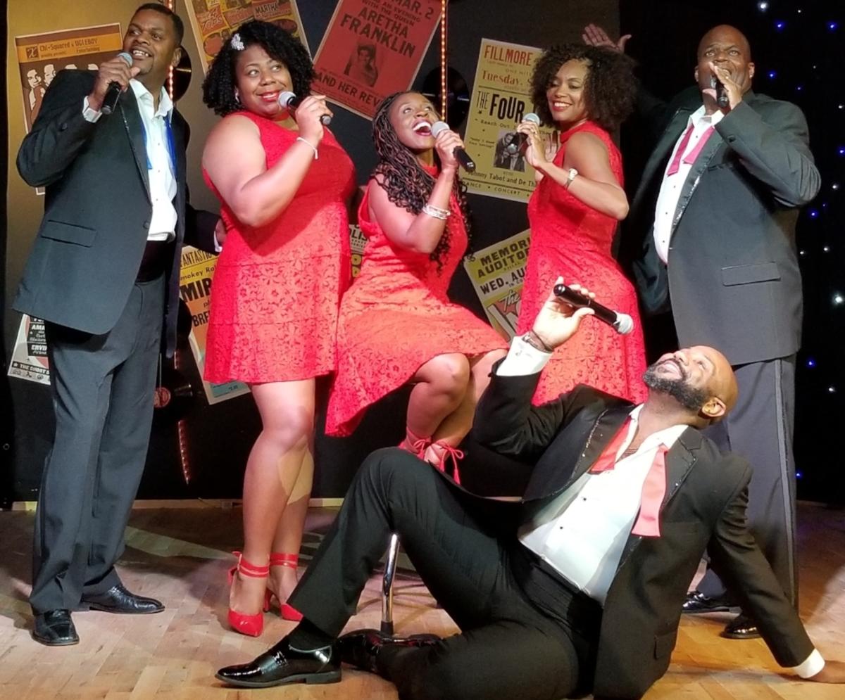 Three women in red dresses and two men in suits sing into microphones during GTS Theatre Motown Christmas