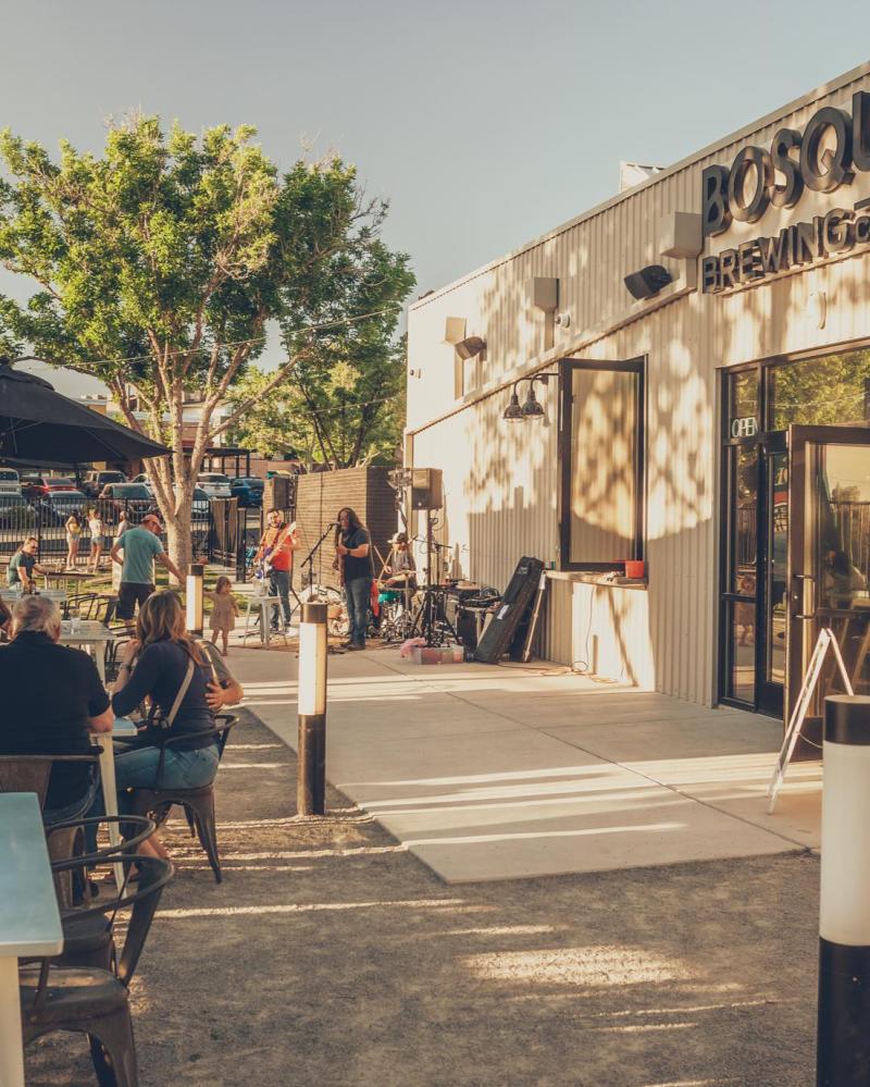 An outside look at the Heights location of Bosque Brewing Company. Patrons drink and listen to live music.
