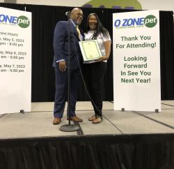 Marie Lee Driver stands on stage with a man in a suit. She poses while holding a certificate