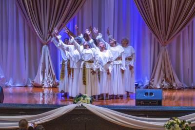 Older dancers stand in cluster with arms raised at an angle.