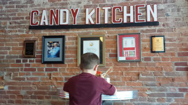 A boy sits at a table at the Martinsville Candy Kitchen in front of historic photos and awards. 