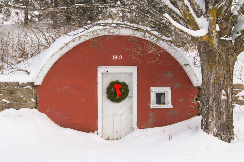 An old red root cellar with a Christmas wreath during a snowstorm.
