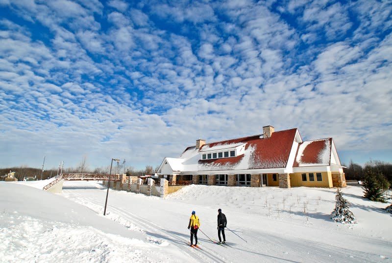 Two people cross-country skiing past the Chalet at Elm Creek Park Reserve