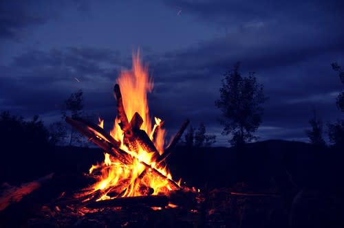 A large bonfire set against a midnight blue night sky with only black outlines of trees visible in the distance