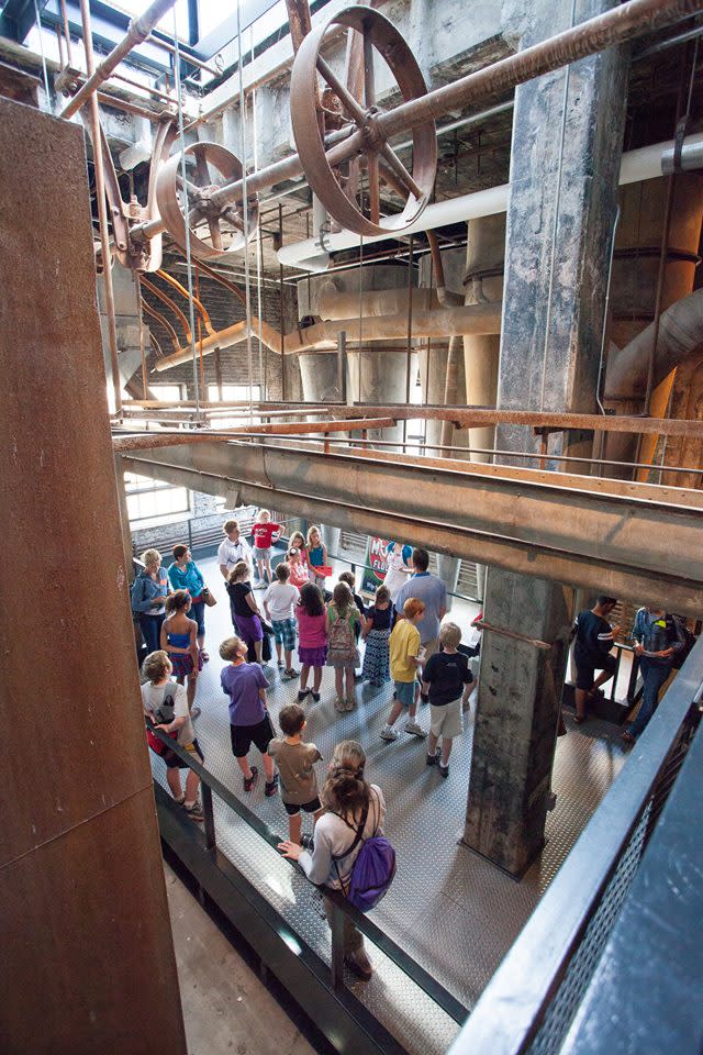 Old-fashioned gears and axels on display above a room of children at the Mill City Museum