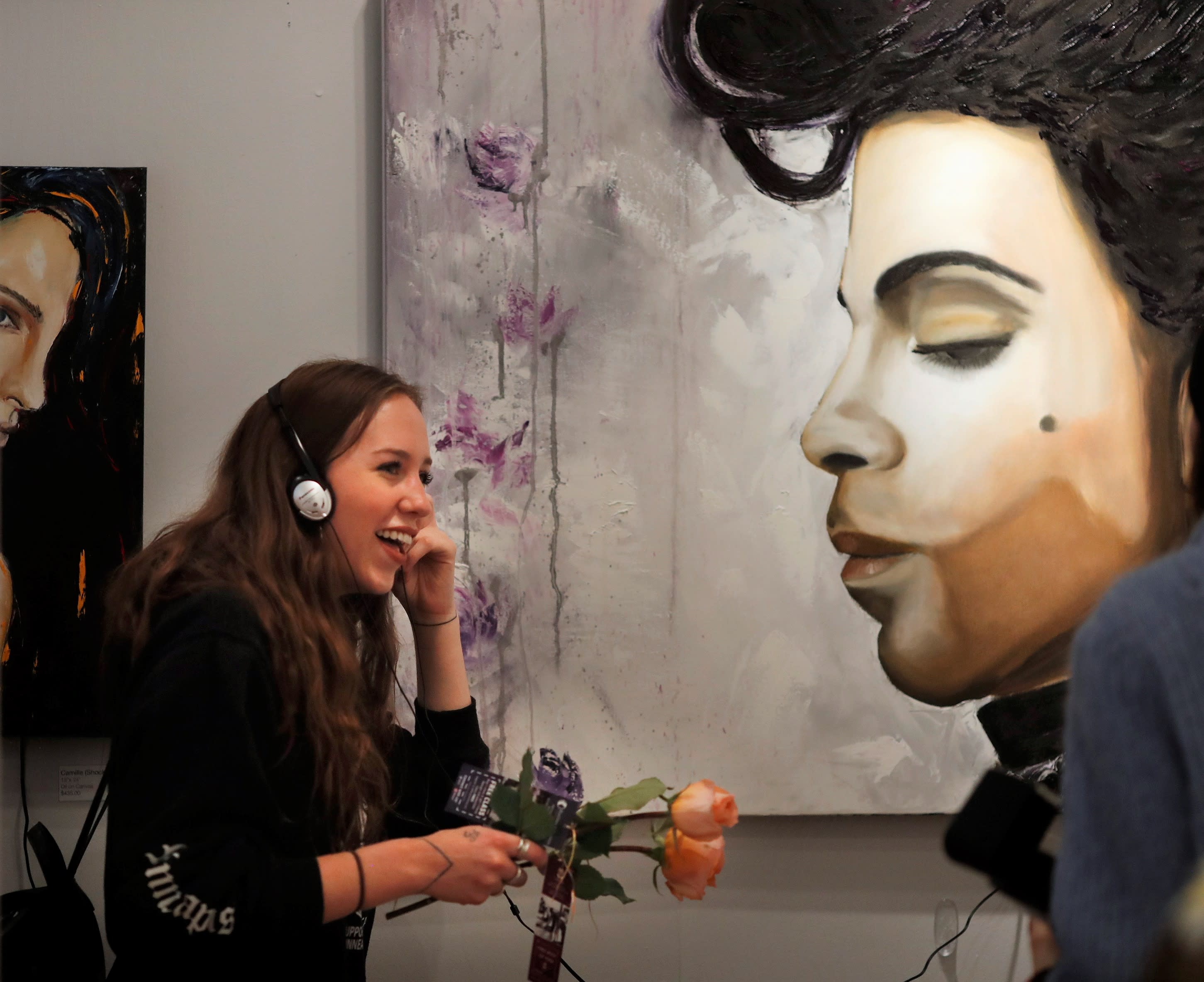 Women standing near large painting of Prince