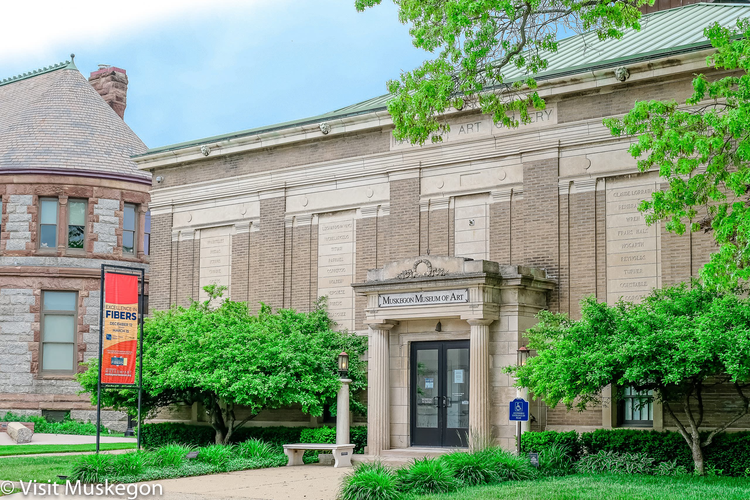 muskegon museum of art entrance; Classical Revival structure with columned portico. a bright sign sits in front with green trees. 