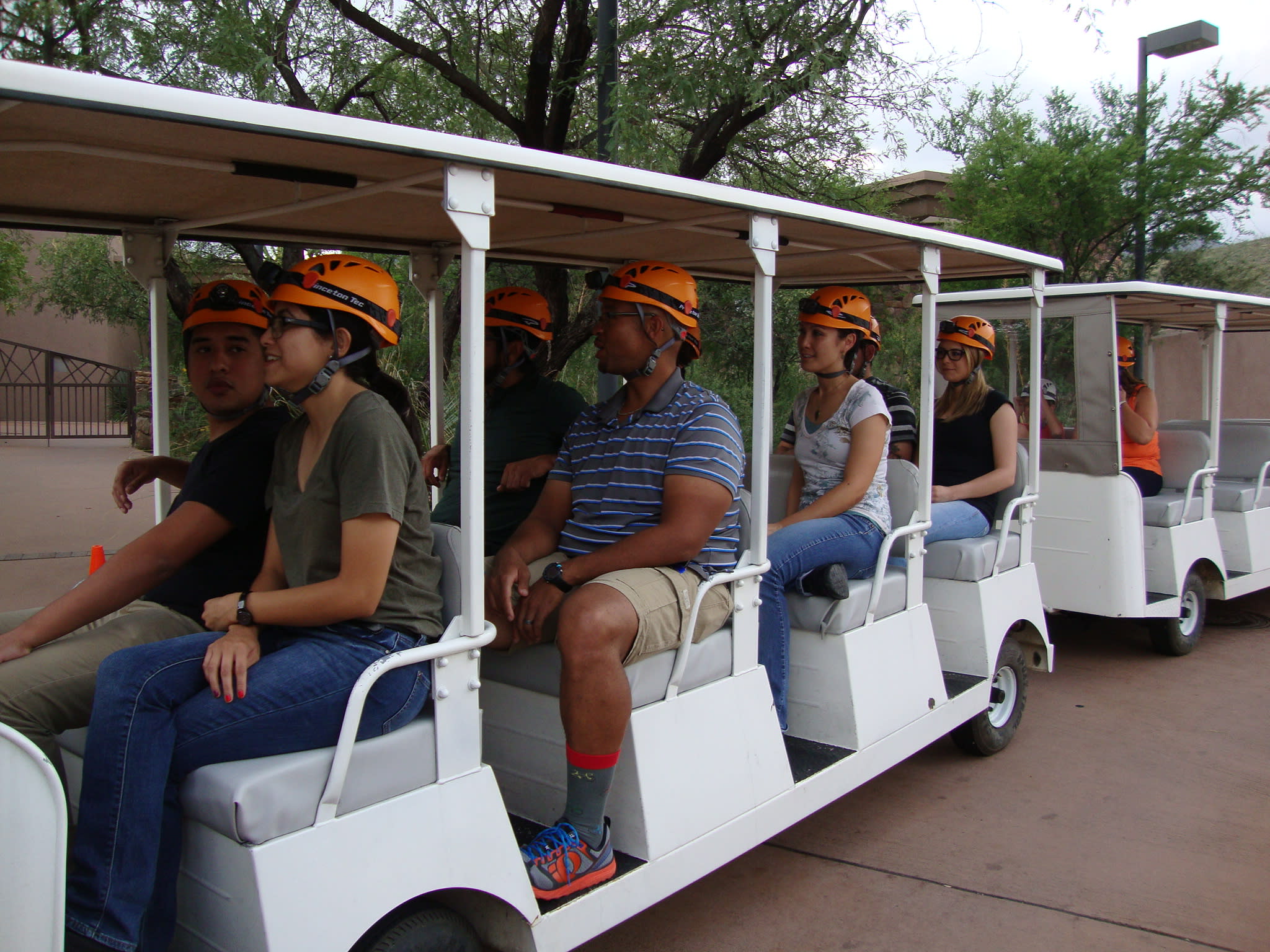 Group of people in orange helmets with headlights sitting on a white open-air tram