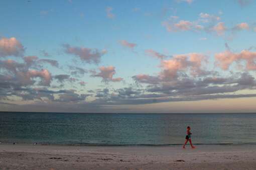 A lone beach walker enjoys a Gulf of Mexico sunrise and its rainbow of hues on Anna Maria Island, where the Bradenton Beach Scenic Highway runs parallel to the water.