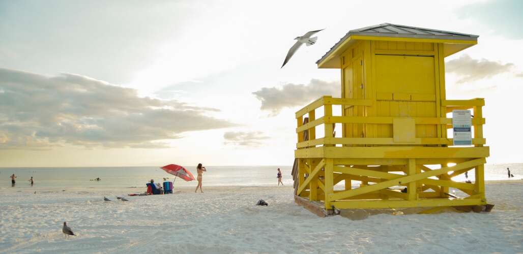 a yellow lifeguard post surrounded by visitors facing the sunset at siesta key beach in sarasota county