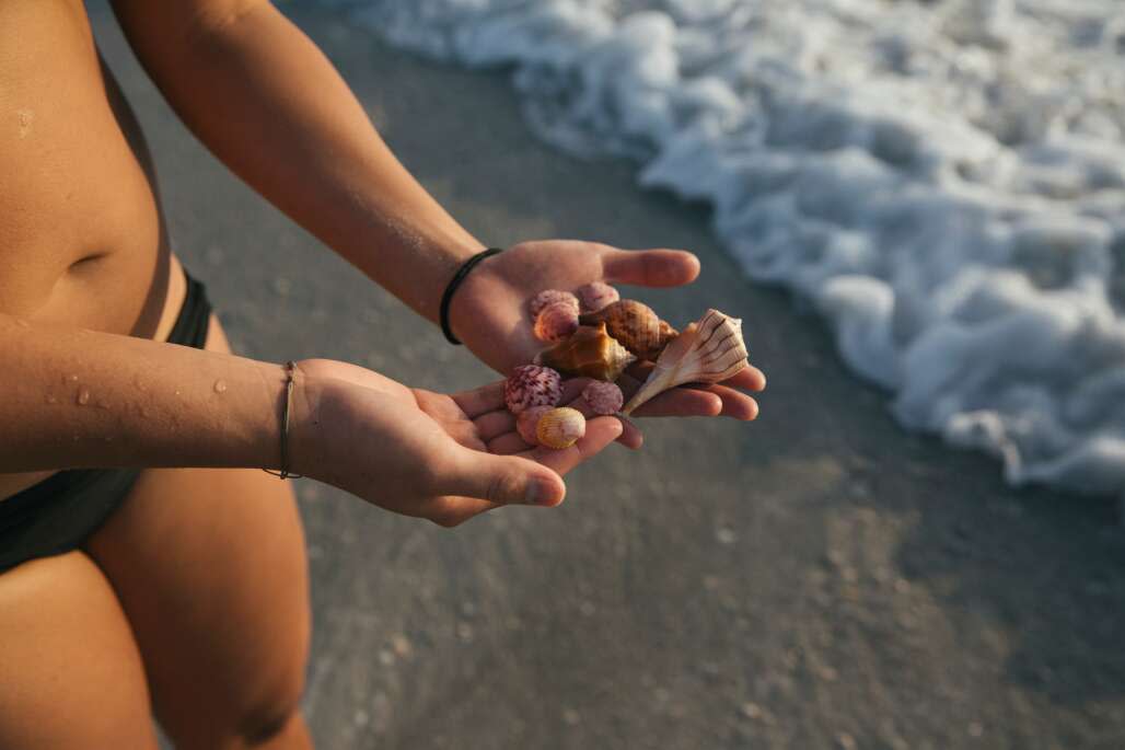 girl holding handful of shells on beach