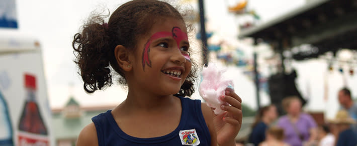 Girl with her face painted eating cotton candy at the state fair