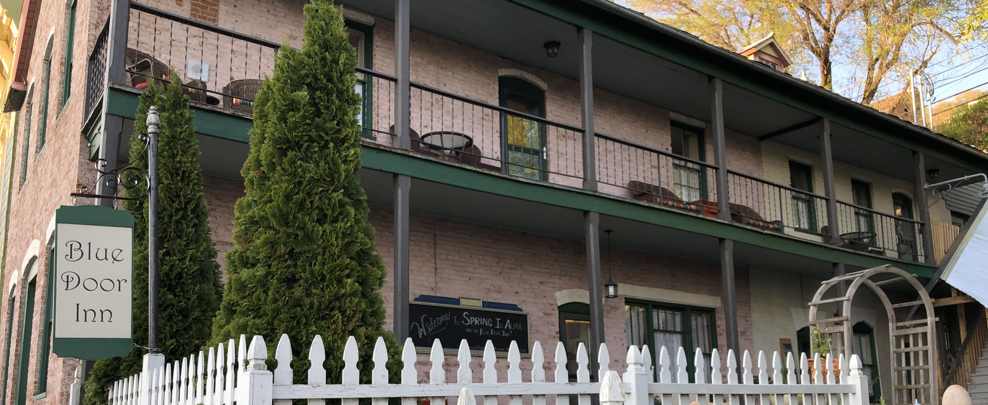 Brick building with white picket fence and an antique sign that reads "Blue Door Inn"