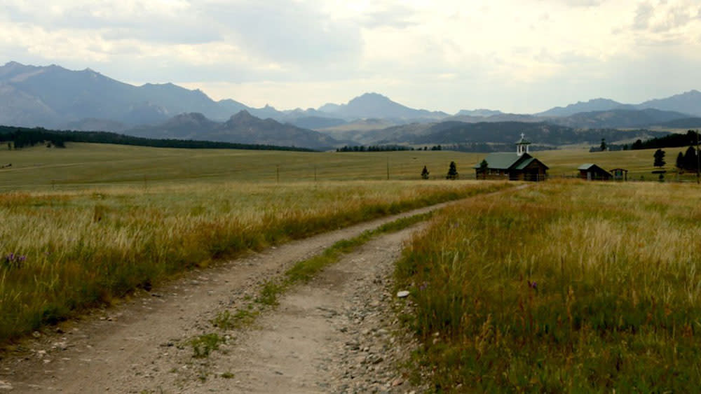 Dirt road through grass pasture with a country church in the background.