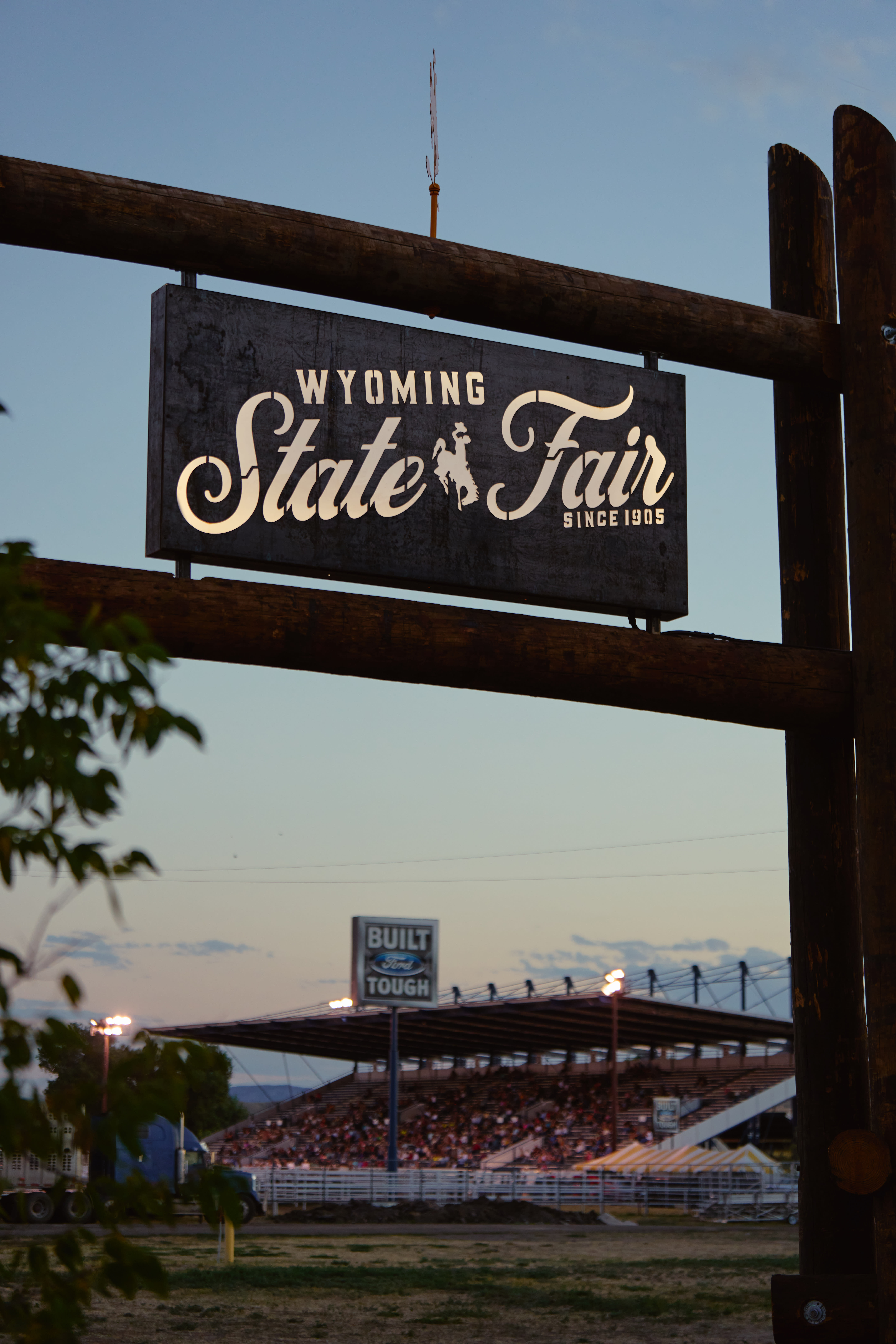 A sign, "Wyoming State Fair" with a backdrop of the fairgrounds at sunset in the background.