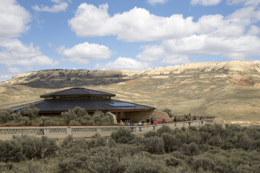 A panoramic view of the landscape circling Fossil Butte National Monument where travelers stand outside the monument visitor center beneath a cloudy sky. 