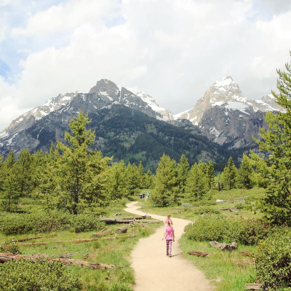 two girls walking down Taggart Lake Trail towards mountains