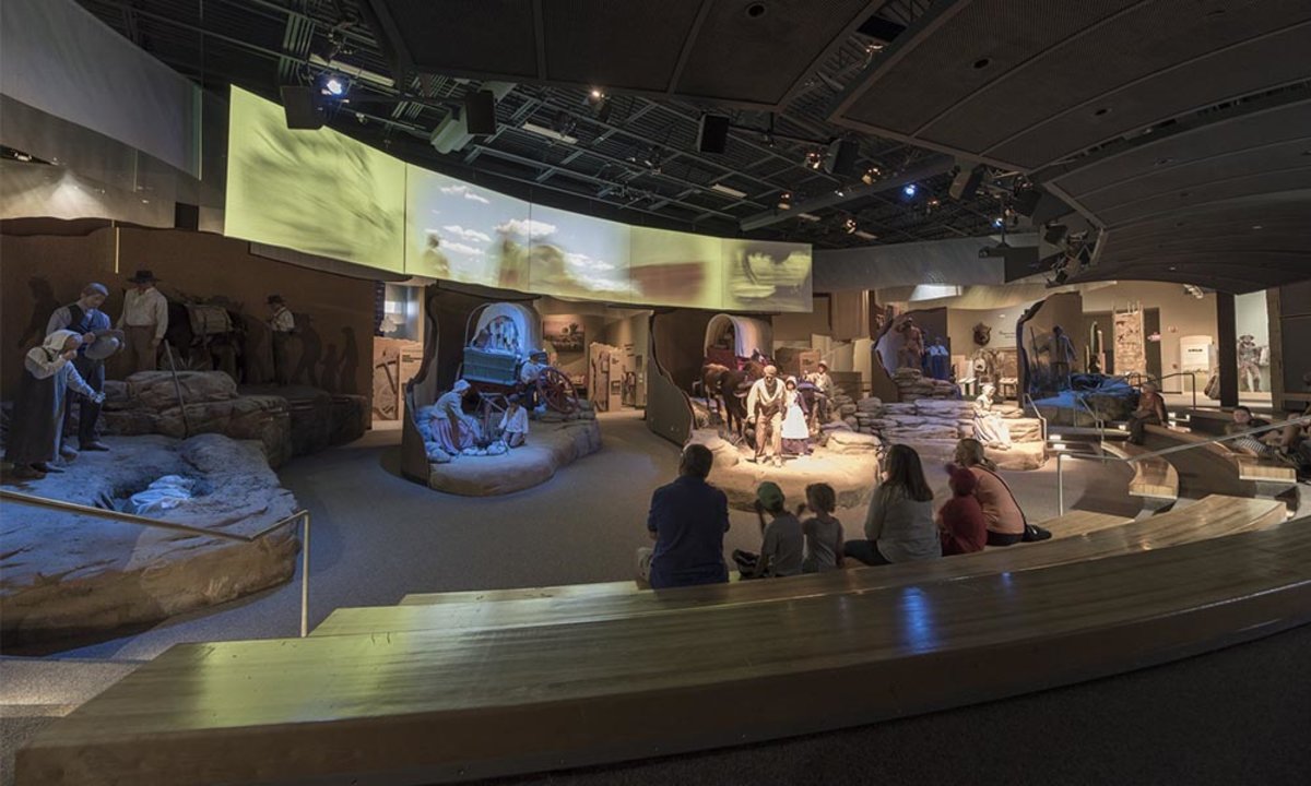 Groups of people sitting down and looking at the various exhibits featuring people and covered wagons depicting pioneer life at the National Historic Trails Interpretive Center.
