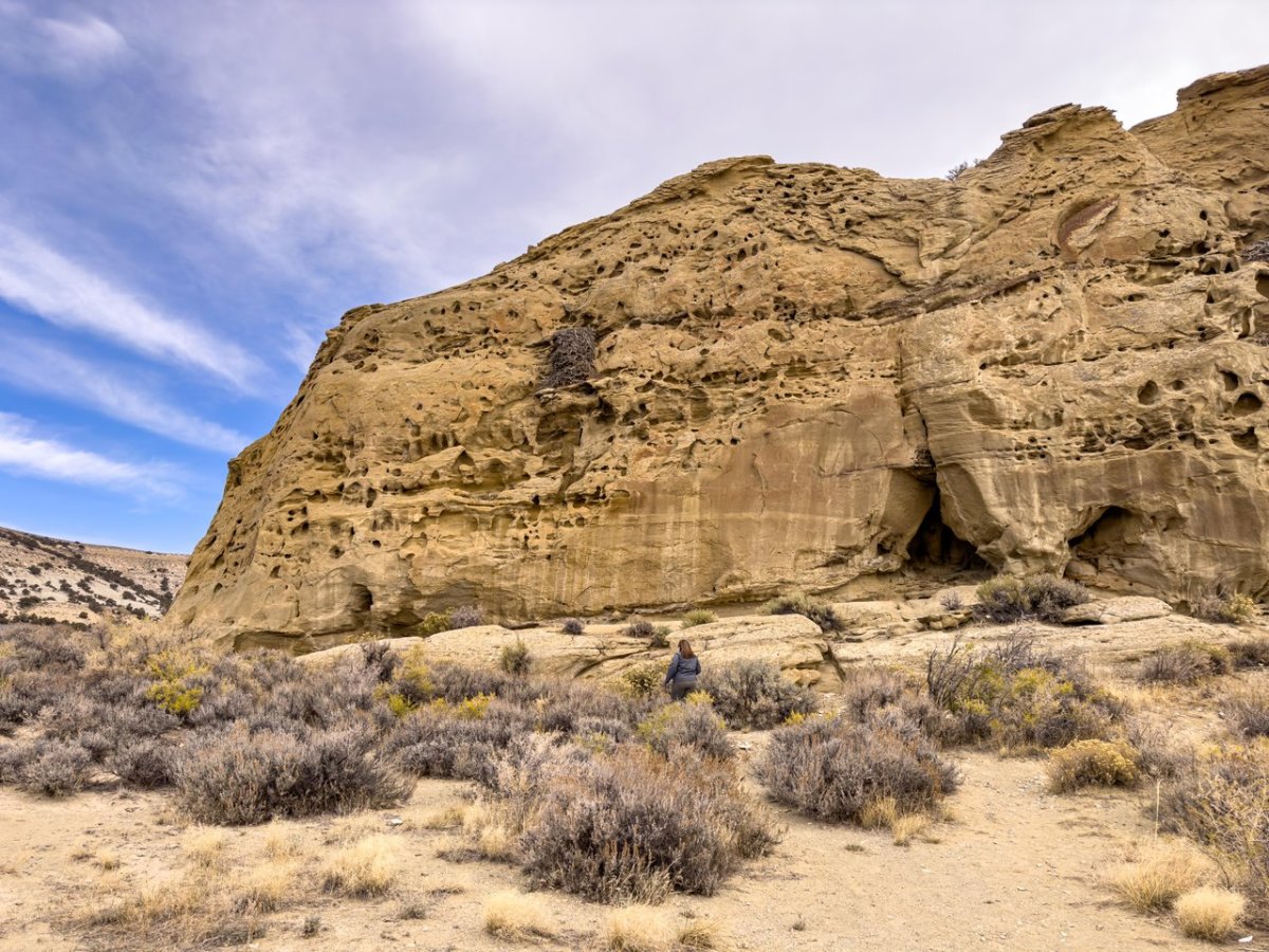 Rugged geologic formations rise high above low bushes in Rock Springs under a cloudy blue sky.