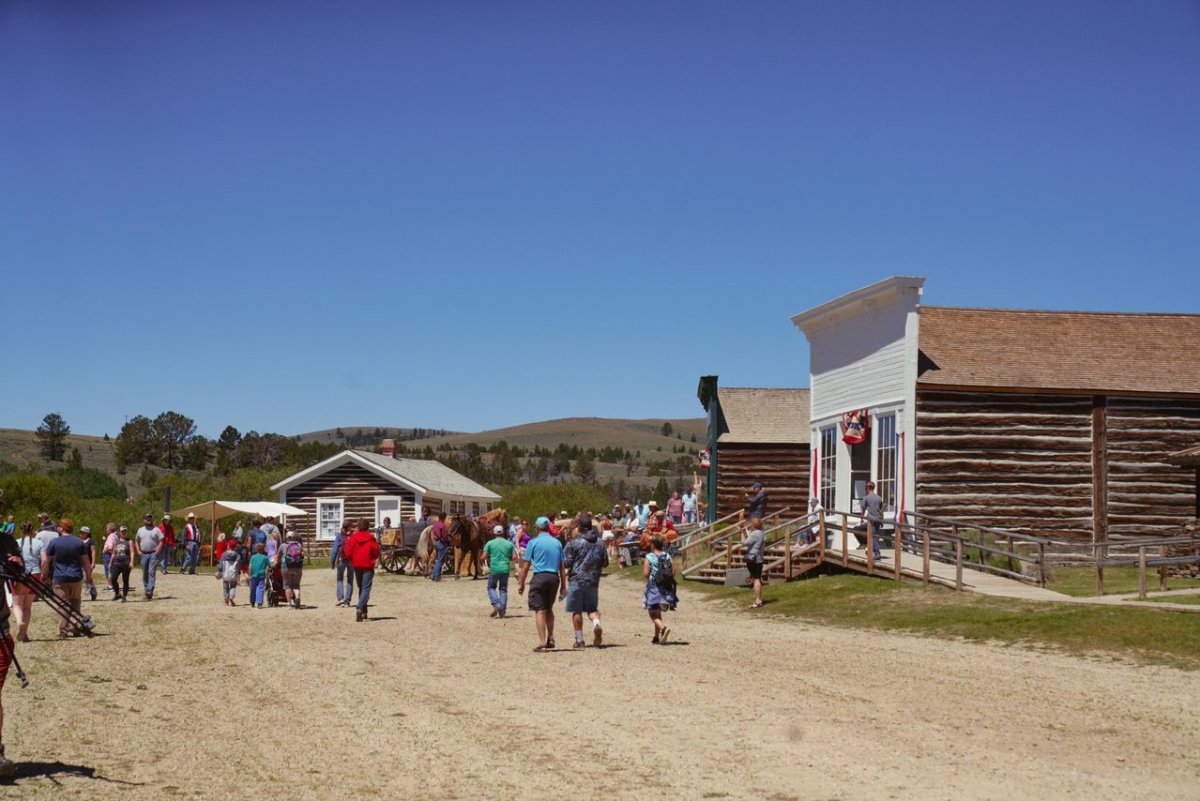 A group of tourists walks toward historic houses at South Pass City, with mountains rising in the distance.