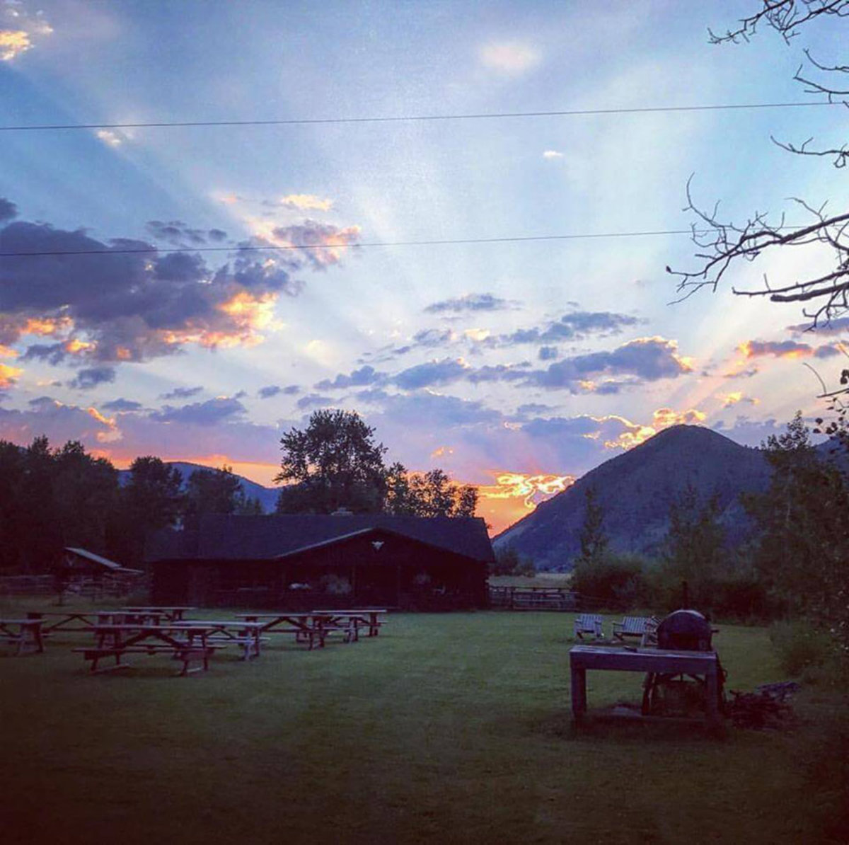 Picnic tables, chairs and a grill in front of  a cabin surrounded by trees and mountains in the background at 7D Ranch.