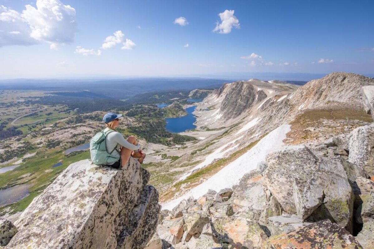 A woman perched on a rock overlooking Medicine Bow Peak and a landscape of trees and lakes at Medicine Bow-Routt National Forests.