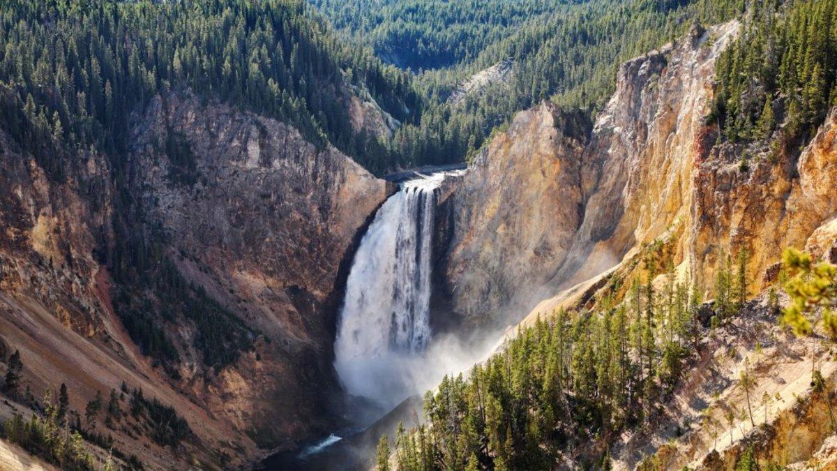 A waterfall cascades down a foliage-decorated canyon, framed by steep cliffs and natural wonder.