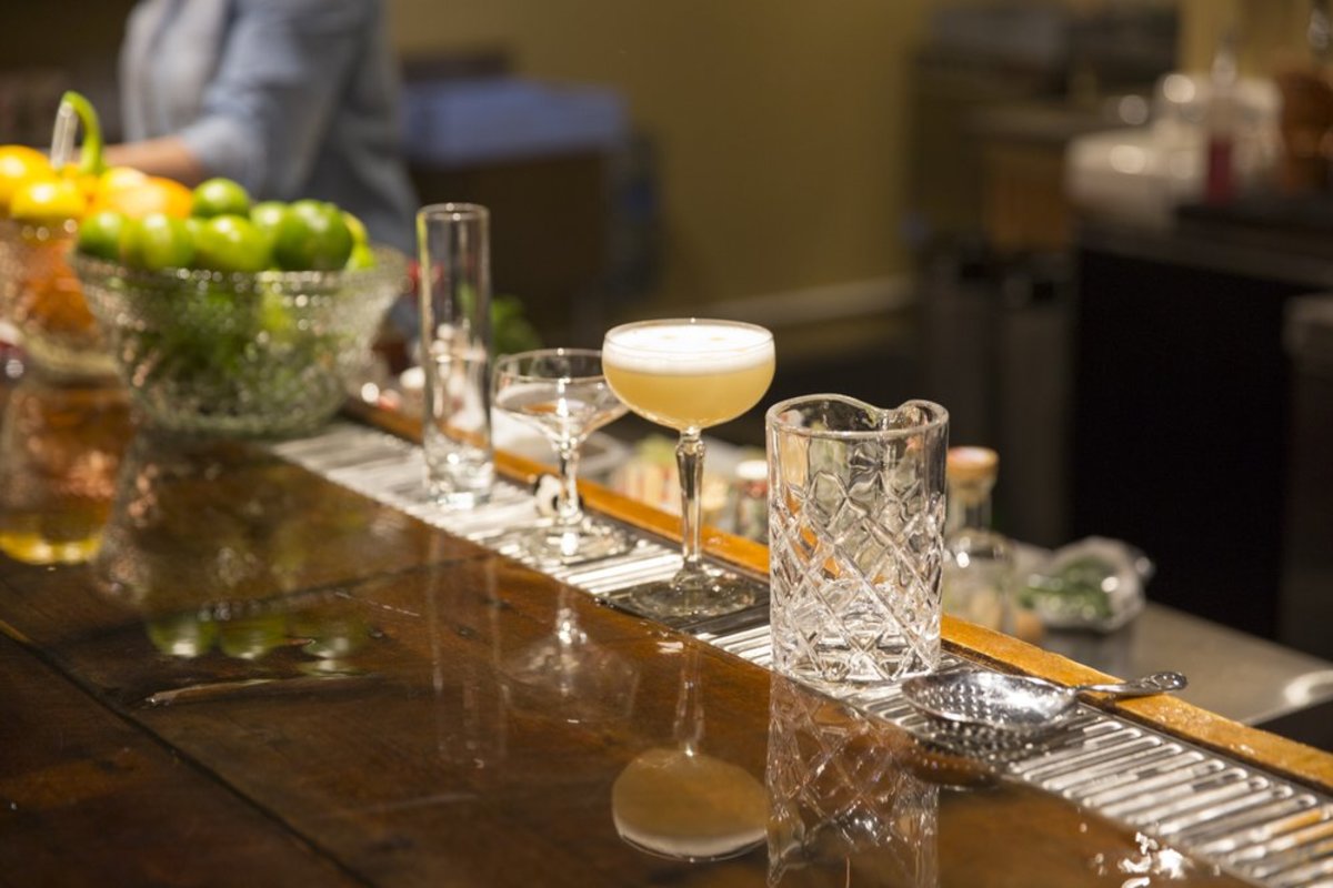 Bowls of fresh citrus and fine glassware line a rustic wood bar top as a bartender serves specialty whiskey cocktails at Backwards Distilling Company in Casper, Wyoming.