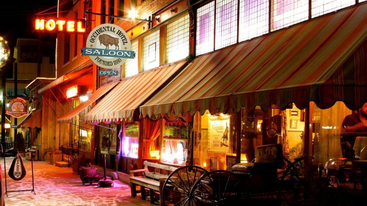 An outside view of the Historic Occidental Hotel Museum with various historic artifacts outside and a sign that reads, "Occidental Hotel Saloon- Founded 1880 - Open."