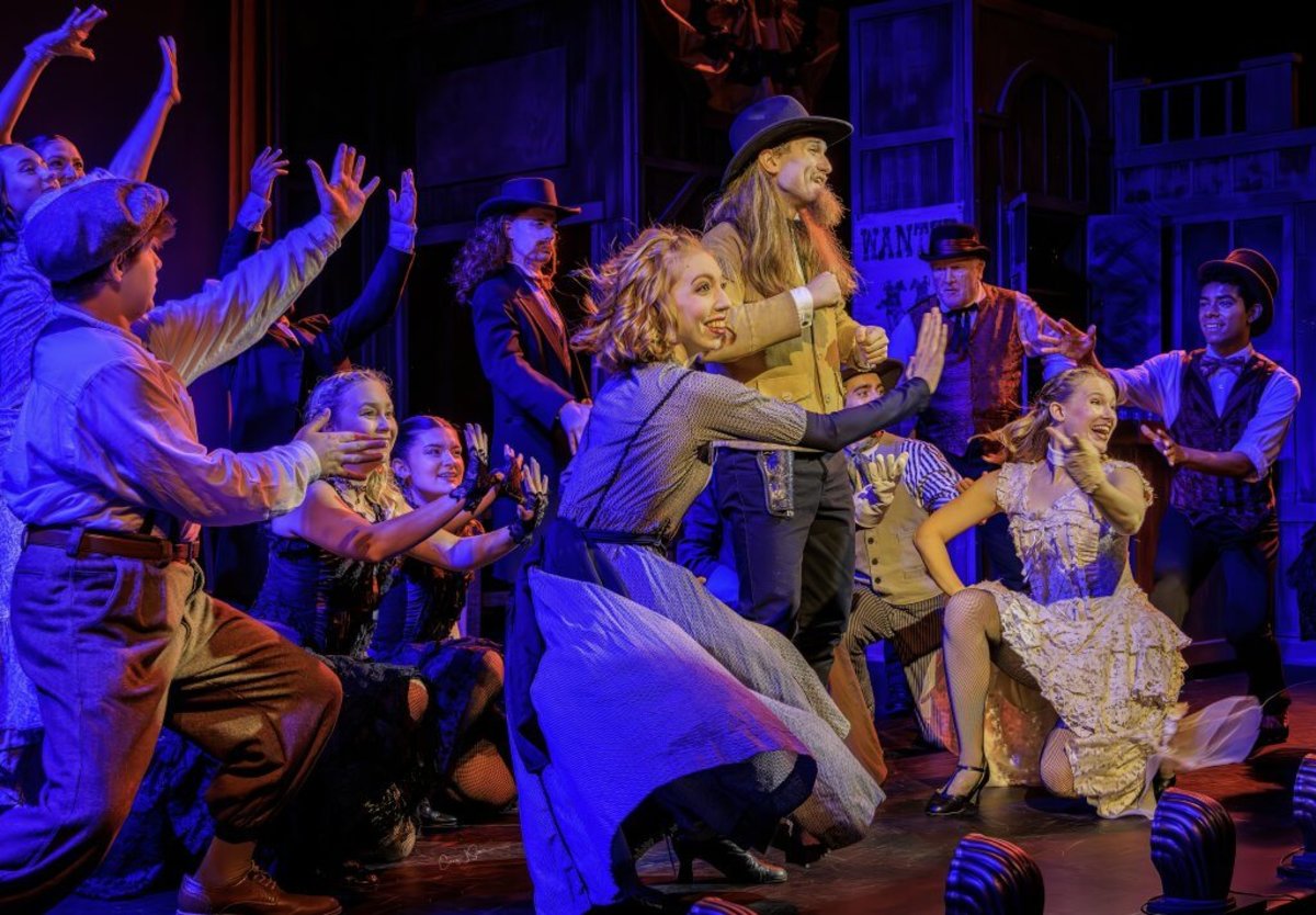 A large group of performers on stage with sets at the Wild West Spectacular show.