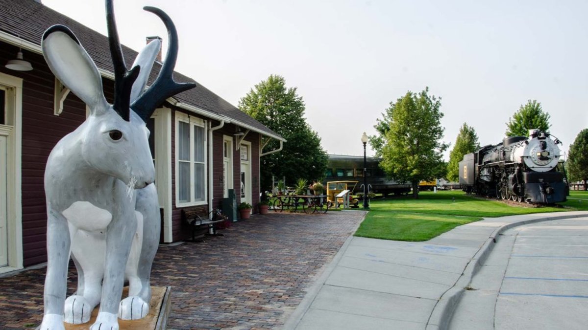 Jackalope statue in front of a building with a train engine behind it in Douglas, Wyoming.